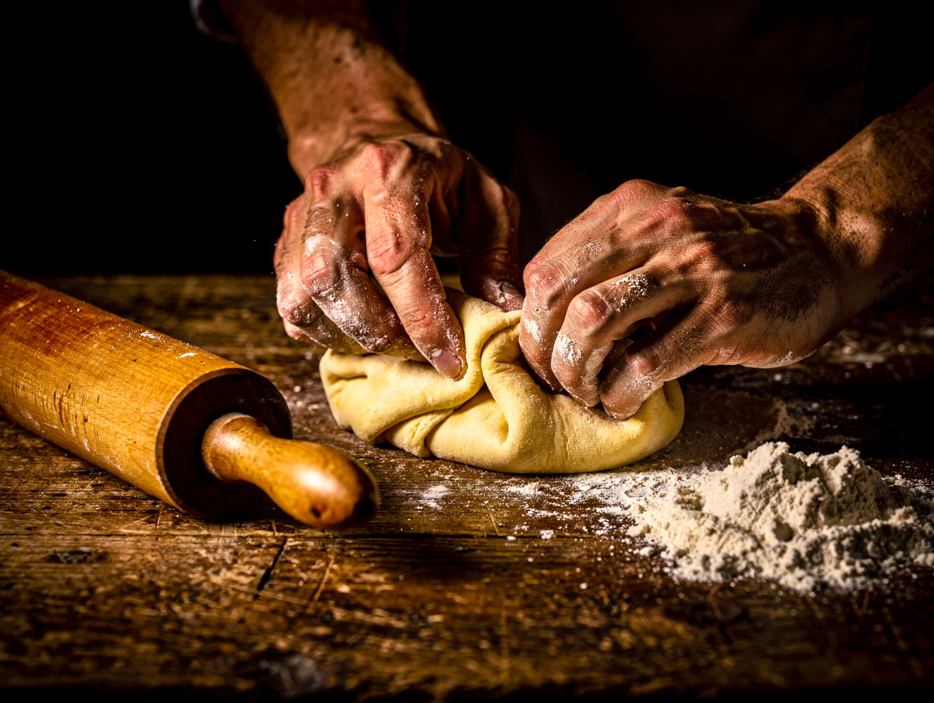 Chef hand-rolling fresh pasta dough on wooden table